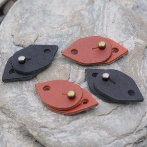 May include: Four leather toggles, two brown and two black, with metal snaps. Each toggle is made of two overlapping pieces of leather.