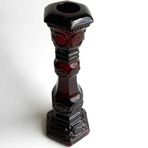 Op de afbeelding: Een donkerrode glazen kaarsenhouder met een zeshoekige basis en een decoratief ontwerp. De houder heeft een brede, open bovenkant voor een kaars.