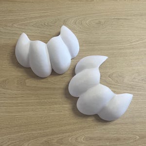 May include: Two white, cloud-shaped decorative pieces. Each piece has a rounded, textured surface with a series of connected, bulbous forms. The objects are placed on a light brown wooden surface.