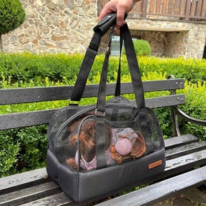 May include: A black pet carrier bag featuring a mesh upper section for ventilation and a solid black base. The carrier includes two sturdy black fabric handles and a small rectangular brown label on the lower right side of the exterior base.