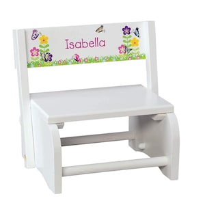 May include: White wooden step stool with a butterfly and flower design. The stool has a personalized name, "Isabella", on the back. The stool has a built-in handle for easy carrying.