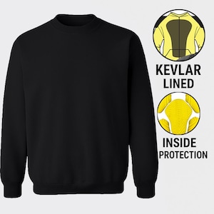 Può includere: Felpa nera girocollo con le parole "KEVLAR LINED" e "INSIDE PROTECTION" in testo bianco. Due illustrazioni circolari mostrano l'interno della felpa con imbottitura protettiva gialla e nera.