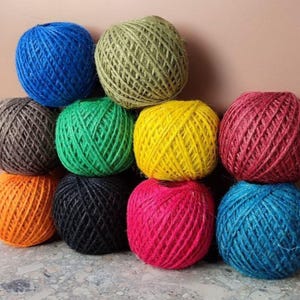Op de afbeelding: Een verzameling kleurrijke touwballen in tinten blauw, groen, geel, rood, oranje, zwart en roze. De ballen zijn gestapeld en tonen hun textuur en levendige kleuren. Ideaal voor knutsel- en decoratieprojecten.