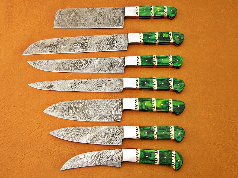 May include: Set of seven kitchen knives with patterned steel blades and green handles. The handles have a decorative design with gold-colored accents. The knives are arranged on a brown surface.