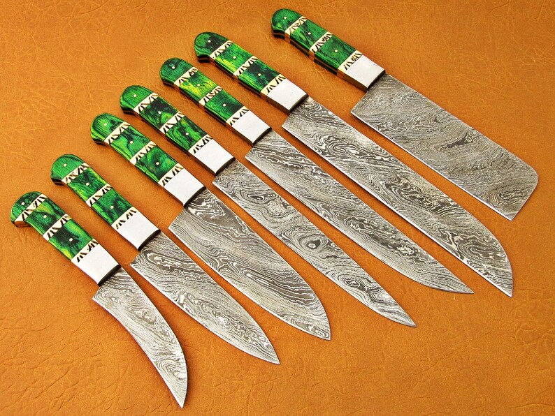 May include: A set of seven Damascus steel knives with green and white handles. The blades have a unique swirling pattern. The handles are a vibrant green with white accents. The knives are arranged diagonally on a brown surface.