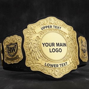 Może przedstawiać: Złoto-czarny pas mistrzowski z ozdobnymi detalami. Pas posiada dużą centralną płytę z miejscem na logo, flankowaną przez dekoracyjne płyty boczne. Obszary tekstowe to "UPPER TEXT" i "LOWER TEXT".