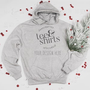 Op de afbeelding: Een grijs hoodie met de tekst "HANDCRAFTED tee&shirts WISCONSIN YOUR DESIGN HERE" bedrukt op de voorkant. De hoodie ligt op een wit oppervlak met rode en witte decoratieve ballen eromheen.