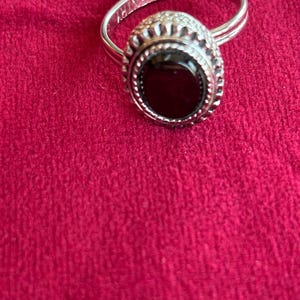 May include: Silver ring with a large, oval black stone. The ring has a decorative bezel setting and a band with the word "COVENTRY" engraved on it. The ring is set against a red background.