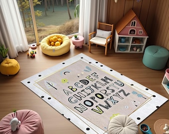 May include: A rectangular rug with the alphabet printed in a playful font. The rug has a light beige background with a gold border and black polka dots. The room also features a pink pouf, a yellow beanbag, and a wooden chair.