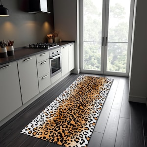 May include: A rectangular leopard print rug in a kitchen setting. The rug features a pattern of black spots on a white and orange background. The rug is placed on a dark wood floor in front of a window.
