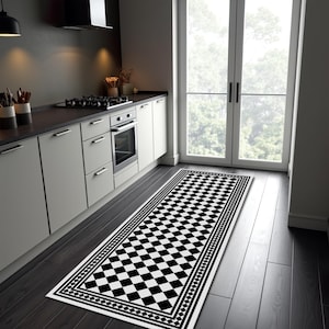 May include: A black and white checkered kitchen runner rug with a decorative border. The rug is rectangular and placed on a dark wood floor in front of a kitchen counter and stove. The rug's pattern is a classic checkerboard design.