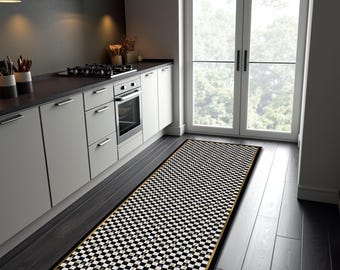 May include: A long, rectangular runner rug featuring a black and white checkered pattern with a thin gold border. The rug is positioned on a dark wooden floor in a kitchen setting, extending from the cabinetry toward a glass door.