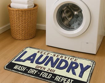 May include: A rectangular laundry room rug with the words "SELF-SERVICE LAUNDRY" in blue and white. The rug also says "WASH - DRY - FOLD - REPEAT" and "OPEN 24H". A white washing machine and a wicker laundry basket with white towels are in the background.