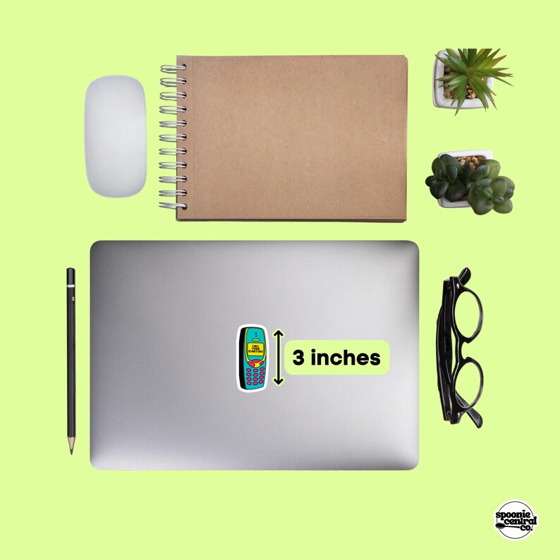 A neatly arranged workspace on a lime green background features a closed laptop with a sticker of a blue and yellow 2000's style phone that says "CALL YOUR SENATORS" labeled 3 inches, a notebook, pencil, mouse, eyeglasses, and small potted plants.