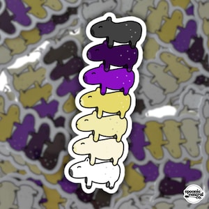 Puede incluir: Una pegatina con una pila de seis capibaras de dibujos animados en varios colores: negro, morado, amarillo y blanco. La pegatina tiene un borde blanco y el texto "spoonie central co." en la esquina inferior derecha.