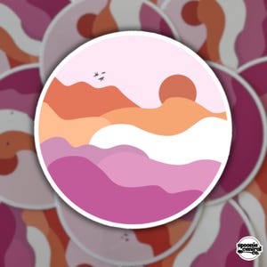 Puede incluir: Una pegatina redonda con un diseño de paisaje en tonos rosa, naranja y blanco. El diseño incluye un sol, montañas y pájaros. La pegatina tiene un borde blanco y el texto "spoonie central co." en la esquina inferior derecha.