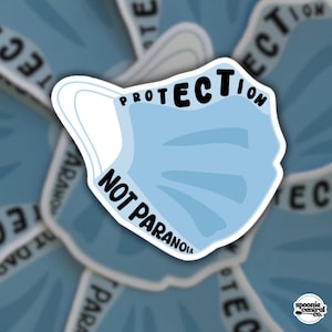 May include: A light blue sticker with a cartoon face mask design. The sticker has the words "PROTECTION" and "NOT PARANOIA" in black. The sticker has a white border and is set against a blurred background of similar stickers.