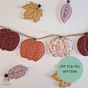 Könnte beinhalten: Eine Girlande aus Stoffkürbissen und Blättern in verschiedenen Mustern und Farben, darunter Orange, Braun und florale Drucke, aufgehängt an einer Jutekordel. Ein grüner Kreis zeigt den Text PDF DIGITAL PATTERN.