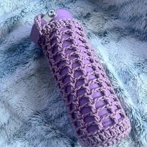 Puede incluir: Una funda de botella de crochet de color morado con un logotipo "BROLY" en el lateral.