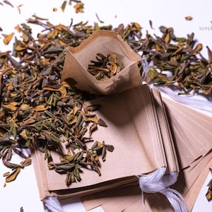 May include: Dried green and brown tea leaves scattered around several brown paper tea bags with white string closures. One tea bag is open, revealing the tea leaves inside. The words "SUPER SPECIAL" are visible in the upper right corner.