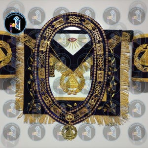 Könnte beinhalten: Ein Satz Freimaurer-Insignien, darunter eine dunkelblaue Samtschürze, ein Kragen und Manschetten, verziert mit goldener Stickerei und Fransen. Die Schürze zeigt ein zentrales Emblem mit einem Auge, und die Manschetten zeigen ein ähnliches Design. Der Kragen ist eine Kette mit einem Anhänger.