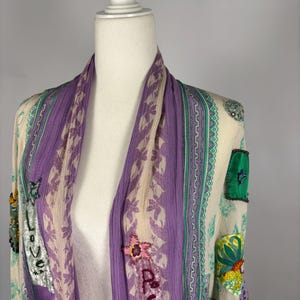 May include: A sheer, open-front kimono in cream, purple, and green. The kimono features floral and geometric patterns, with the word "Love" and "Be You" embroidered on the front. The sleeves have a ruffled hem.