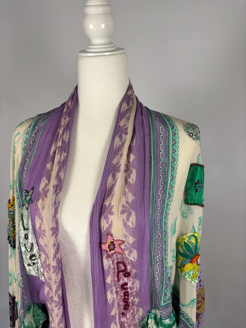 May include: A sheer, open-front kimono in cream, purple, and green. The kimono features floral and geometric patterns, with the word "Love" and "Be You" embroidered on the front. The sleeves have a ruffled hem.