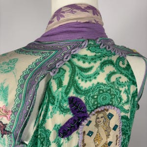 May include: A sleeveless top with a green paisley pattern, accented with purple trim and a decorative patch featuring a woman in a gold dress. A purple scarf is draped around the neck.