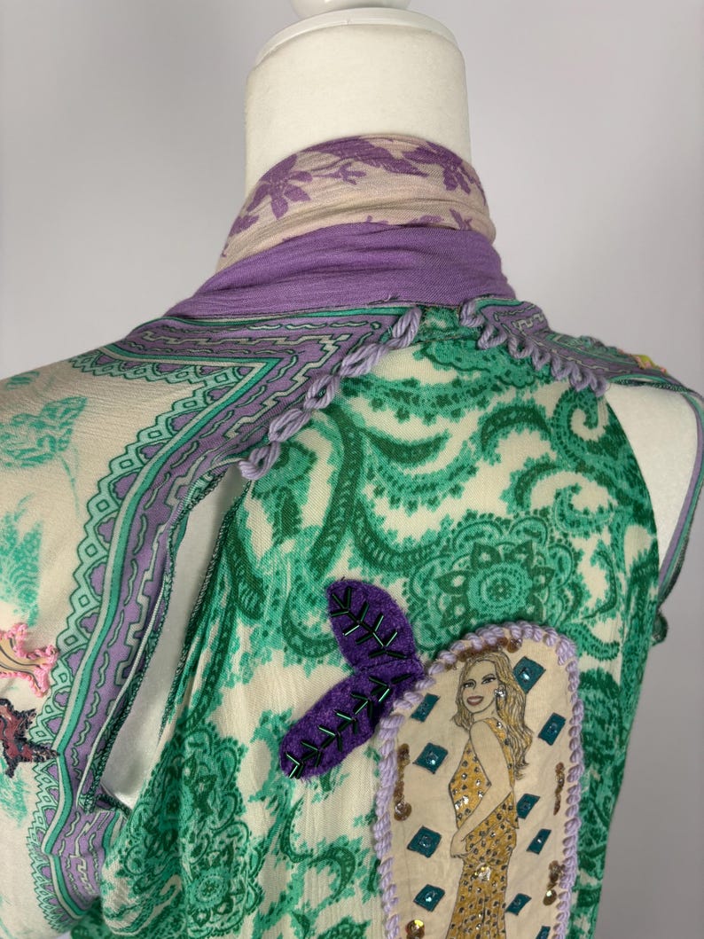 May include: A sleeveless top with a green paisley pattern, accented with purple trim and a decorative patch featuring a woman in a gold dress. A purple scarf is draped around the neck.