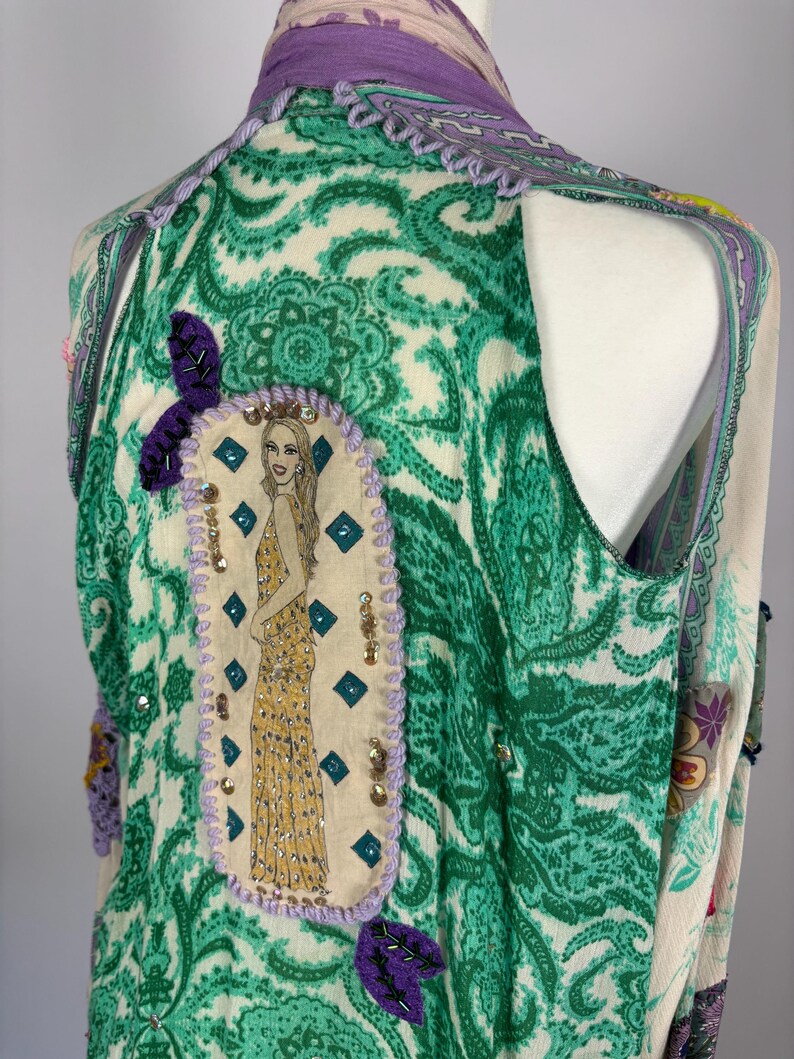 May include: A sleeveless vest with a paisley pattern in green and cream. The vest features a purple trim and a decorative patch with a woman in a yellow dress. The vest is adorned with sequins and purple leaf accents.