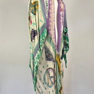 May include: A long, flowing kimono in cream, green, and purple. The kimono features various patches with designs like hearts, peace signs, and the word "LOVE". It has a decorative tassel and is displayed on a mannequin.