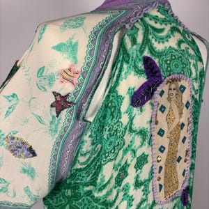 May include: A patterned, long-sleeved garment with a green and white paisley design. The garment features a purple collar and trim, with decorative patches and embellishments. A patch with a woman in a gold dress is on the back.