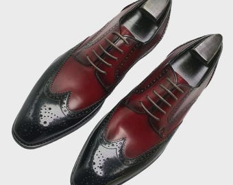 May include: A pair of two-tone leather dress shoes. The shoes have a burgundy vamp and quarter, with black toe caps and wingtip detailing. Brown laces and shoe trees are visible.