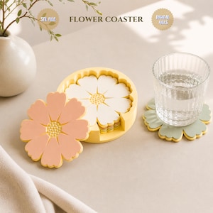 Op de afbeelding: Een set bloemvormige onderzetters in perzik, wit en groen, met een gele houder. Een glas water staat op een van de onderzetters. De tekst "FLOWER COASTER" is zichtbaar.