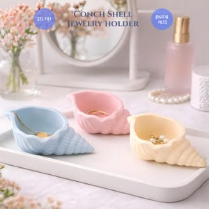 May include: Three conch shell jewelry holders in pastel colors: light blue, pink, and yellow. Each shell is on a white tray and holds jewelry. The text reads "CONCH SHELL JEWELRY HOLDER", "STL FILE", and "DIGITAL FILES".
