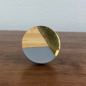 May include: A round wooden knob with a geometric design. The knob is made of wood, painted gray and gold.