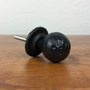 Puede incluir: Pomo de hierro fundido negro con un dise&ntilde;o redondo y texturado. El pomo tiene un tornillo plateado para sujetarlo a una superficie.
