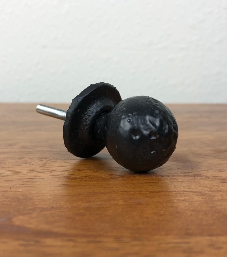 Puede incluir: Pomo de hierro fundido negro con un dise&ntilde;o redondo y texturado. El pomo tiene un tornillo plateado para sujetarlo a una superficie.