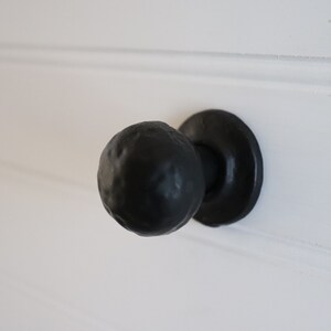 Puede incluir: Pomo de puerta negro con una manija redonda texturizada y una base circular plana.
