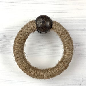 May include: A brown wooden bead ring with a thick rope of natural jute twine. The ring is a simple, rustic design.