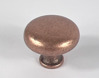 May include: A copper-colored cabinet knob with a rounded top and a short, cylindrical base. The knob has a textured surface and a slightly aged appearance, suggesting a vintage or rustic style. The hardware is designed for use on drawers or cabinet doors.