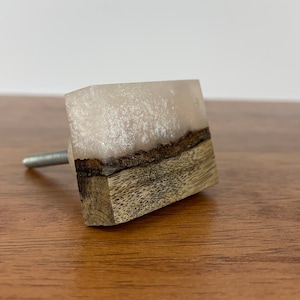 May include: A white and brown rectangular cabinet knob with a silver screw. The knob is made of resin and wood.