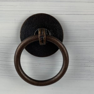 May include: A dark brown metal ring pull cabinet knob with a round base.