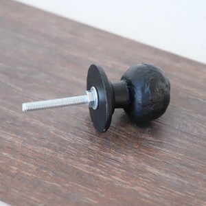Puede incluir: Pomo de armario de metal negro con forma redonda y un tornillo para la instalaci&oacute;n.