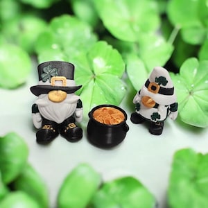 May include: Two St. Patrick's Day gnomes with a pot of gold. One gnome wears a black top hat with a shamrock, the other a white hat. The pot is black and filled with gold coins. The background is green clover.