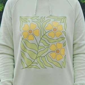 Sudadera verde claro "Encuéntrame en los prados", diseño floral fluido, sudadera con estampado primaveral, texto caligráfico, estilo suave, Stanley/Stella