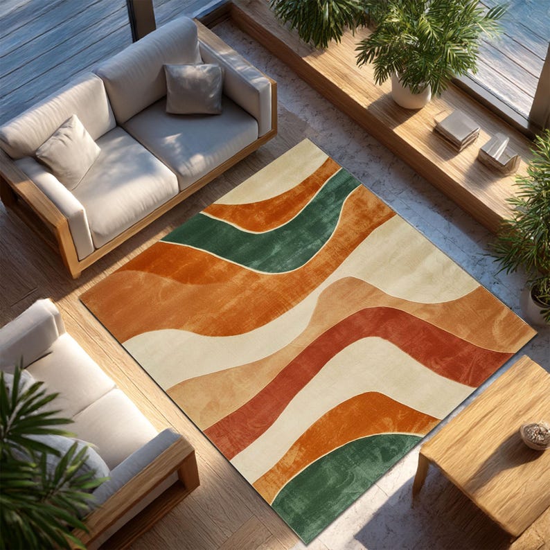 May include: A rectangular area rug with an abstract design of flowing, layered bands in shades of orange, green, and cream. The rug is placed on a wooden floor, with two sofas and a small table visible in the background. The rug's design adds a modern touch to the room.