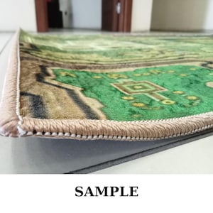 May include: Close-up of a green and tan patterned rug with a beige border. The rug features a detailed design with geometric shapes and a textured surface. The word "SAMPLE" is printed at the bottom.