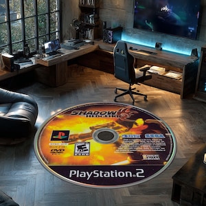 Puede incluir: Alfombra redonda con el diseño de un disco de juego de PlayStation 2 para "Shadow the Hedgehog". La alfombra tiene un fondo amarillo y naranja con el logotipo y el arte del personaje del juego. El texto "PlayStation 2" está impreso en la parte inferior.
