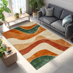 May include: A rectangular area rug with a wavy pattern in shades of orange, green, and cream. The rug is placed on a light-colored floor in a living room setting, with a gray sofa and wooden furniture visible.